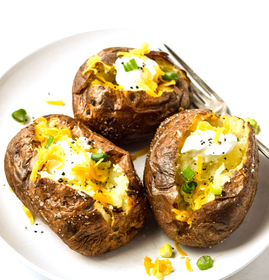 air fried baked potatoes on plate topped with cheese, sour cream, and chives