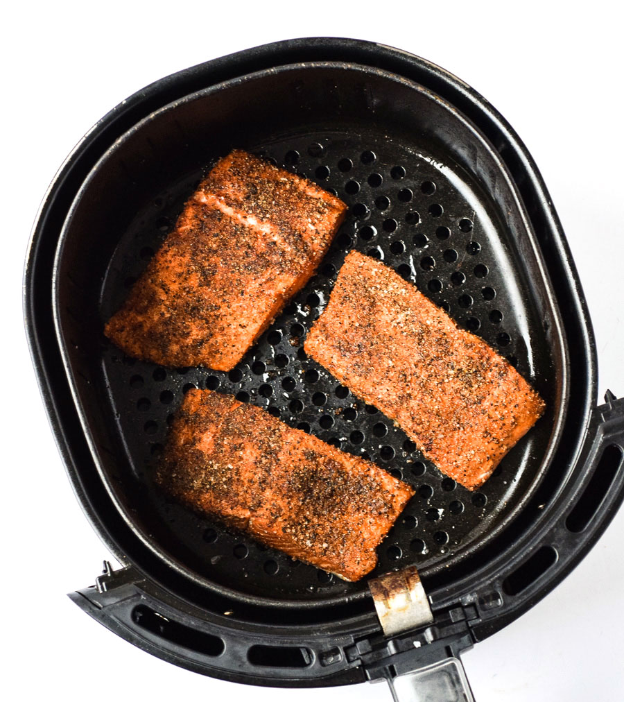 salmon filets in air fryer basket with blackened seasoning