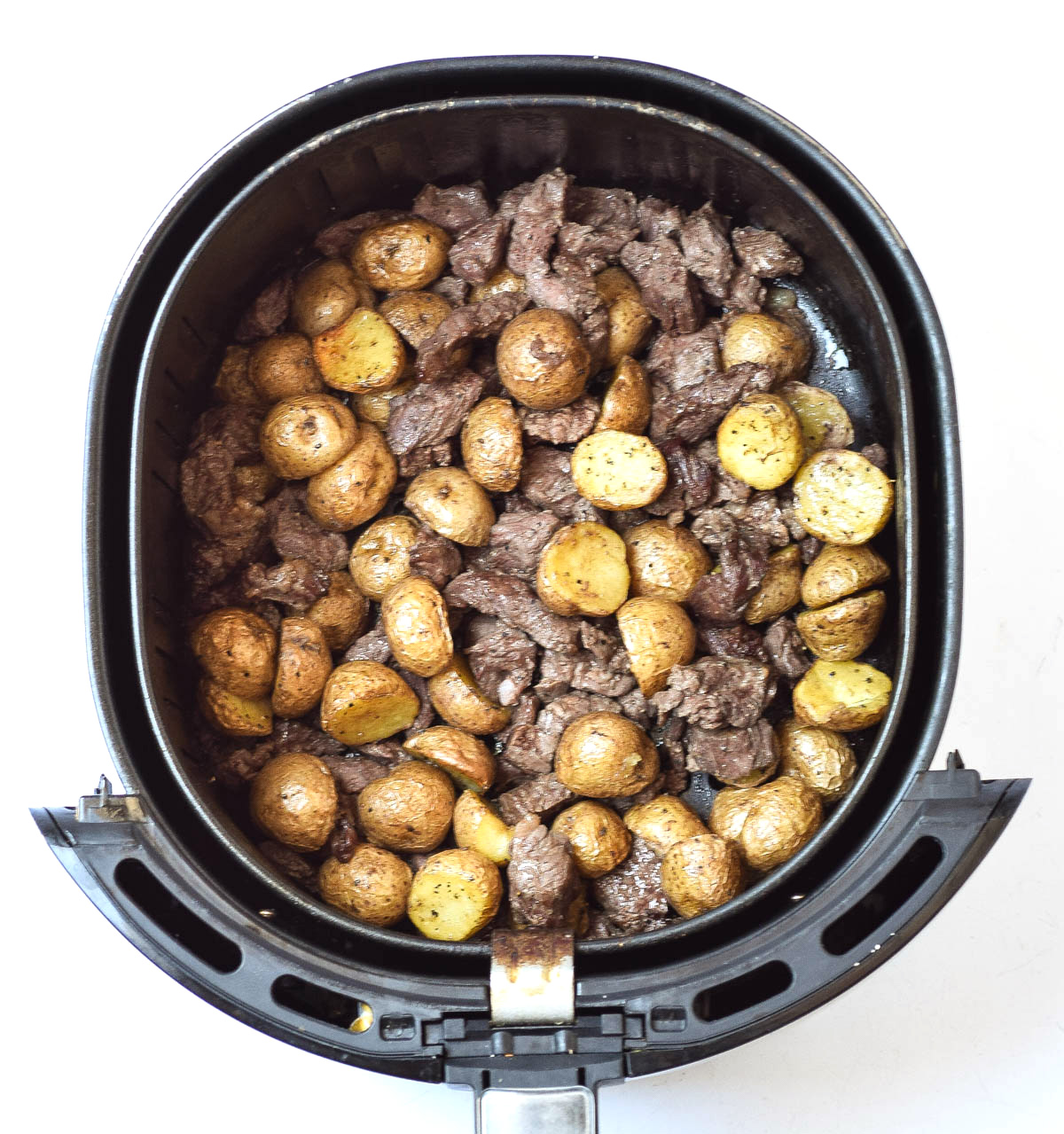 steak bites and potatoes in air fryer basket after cooking
