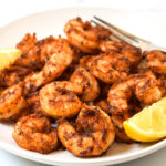 blackened shrimp piled on a plate with lemon wedges