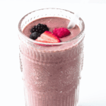 tall clear glass of high protein berry smoothie with fresh berries on top